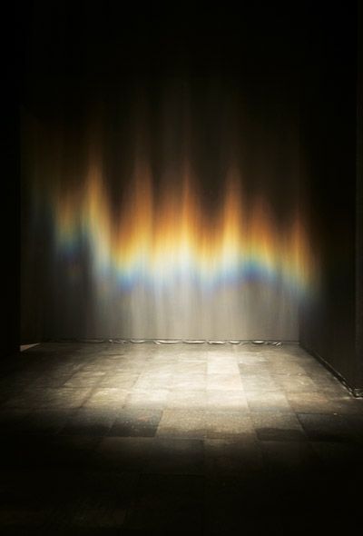 Beauty (1993). From the exhibition Take your Time: Olafur Eliasson, installation view at San Francisco Museum of Modern Art. Gently falling mist from the overhead sprinklers produce iridescent effects as the light is diffracted on the tiny droplets of water as it descends. Other than the light and the mist the room is empty.