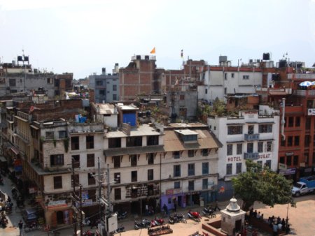 En général, les avions de ligne volent à environ 10 000m, donc, de là-haut, on ne voit qu'une mer de nuages. En arrivant au Népal, face à la chaîne de l'Himalaya, on peut nettement apercevoir le sommet des montagnes dépassant des nuages, tel un rempart ! A l'orée des montagnes : Kathmandou. Vue du ciel c'est un amas de maisons basses couleur de terre agglutinées dans une large vallée enveloppée de brume. L'aéroport est proche. Dehors, la chaleur est tropicale. Nous embarquons rapidement dans un petit car pour traverser la ville. Les rues y sont étroites. On zigzague constamment entre vélos, petites autos, camions, petits cars et passants. Tous se croisent maladroitement, mais à faible vitesse et sans stress. On s'accommode du trafic. Et de toute manière les véhicules ne sont pas récents. La première impression que j'en ai eue, c'est un dédale de routes en terre avec quelques endroits de macadam, de maisons brunes en bois, tôle, parpaings. De nombreuses boutiques occupent les façades, placardant surtout des boissons gazeuses en canettes, paquets de chips, souvenirs pour touristes (statuettes, bols à prière, bijoux, draperies…) mais aussi de l'équipement pour les randonneurs, signes qui montrent que l'occident est aussi présent dans la capitale de ce pays niché sur les pentes de la plus haute chaîne de montagnes du monde. Ses habitants sont vêtus à l'occidentale et à la vue de touristes, certains passants s'arrêtent pour les observer, proposer des babioles, leurs services ou jouer un morceau de musique pour de l'argent (évidemment) mais sans insister. L'époque de hippies a laissé place à celle du commerce. Les rues grouillent de vie, malgré les fréquentes pannes d'électricité. L'activité décroît vers 21h et devient moribonde une demi-heure plus tard. Le premier repas que nous propose notre guide népalais, Anup, est dans un restaurant en bois de quatre étages, et nous nous asseyons sur des coussins au sol autour d'une table basse, c'est en fin de compte la manière la plus conviviale de manger. Le menu est un « Dal Bhat », le plat national : du riz, une purée de lentilles noires dessus, des légumes verts, de l'agneau au curry, du sanglier, des épinards et des beignets de légumes cuits à la vapeur. Ce soir, c'est la version « de luxe ». Ensuite, on boit de l'alcool de riz versé de haut qui mousse dans un petit bol en terre cuite. Nous sommes un groupe de dix personnes qui se découvre. Les âges des participants varient d'une petite trentaine jusqu'à la retraite. La plupart viennent de villes de province, et deux habitent actuellement en Autriche et en Suisse. Les professions de chacun sont d'horizons variés, avec une dominance d'enseignants. La plupart sont des randonneurs chevronnés, habitués aux pays lointains. Je fais figure de débutant naïf, parfait !