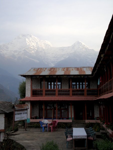 Au matin, la vue sur l'Annapurna Sud, qui surplombe la vallée, est dégagée. On aperçoit également, sur la montagne d'en face, le village où nous nous arrêterons au retour de notre périple. Notre groupe reprend sa marche sur les escaliers d'ardoises, en descente. Nous quittons à nouveau les cultures de riz en terrasse (les pousses sont embryonnaires et les bassins sont rarement remplis) pour entrer à nouveau dans la forêt. Arrivés à la rivière, nous la traversons sur un immense pont suspendu. Le même manège que la veille se produit, immortalisé par quelques séances de photo. Nous arrivons ensuite sur la crête de la montagne d'en face. Le lieu du repas de midi est un petit amas de deux ou trois maisons nichées au sommet. Nous nous posons sur la terrasse qui surplombe la vallée pour nous désaltérer. La plupart d'entre nous repartent vers une rivière pour aller se baigner dans des sources chaudes. Les autres nous attendent là pour le déjeuner, profitant de la présence de tibétains qui vendent des babioles pour exercer leurs talents au marchandage. Nous descendons en direction des sources à vive allure, traversant les rayons du soleil qui perçent la forêt. Il y a ladeux bassins en ardoise, nous nous jetons à l'eau. La température des bassins est de 30 ou 40°, ce qui est fort agréable même sous le soleil cuisant. L'une d'entre nous testera également la température de la rivière ! Cette petite cure thermale me sort de l'ambiance mystique de la forêt, mais nous prenons le temps de discuter. Nous ne pouvons nous attarder trop longtemps et remontons vers le restaurant. C'est plus difficile, l'eau nous a quelque peu ramollis, mais la faim nous tiraille tant et plus… et le reste du groupe nous attend. Après le repas, nous reprenons notre marche à travers l'escalier escarpé en nous pressant: des nuages venus du haut des montagnes recouvrent maintenant la vallée (ce qui devient une habitude l'après-midi). A croire que les éléments nous pressent inlassablement de continuer sans prendre le temps d'en profiter. Nous devons arriver avant la pluie. Au cours de l'après-midi, nous montons jusqu'à l'étape du soir, Chumrung. Notre arrivée est saluée de façon spectaculaire. Notre lodge, tout en haut du village est entourée de nombreuses « guirlandes » de drapeaux à prières bouddhistes, brusquement agitées par un vent violent qui se lève. Les nuages qui sont chahutés découvrent de temps en temps les sommets dans le lointain. La scène a vraiment quelque chose de surnaturel cette fois. La brise rafraîchit l'air depuis peu et notre guide confirme : nous avons gagné en altitude. Fini le climat tropical, c'est maintenant « tempéré » et nous auront prochainement un climat froid de haute montagne. Chic, on se rapproche ! L'étage de la lodge n'a de fenêtres qu'aux chambres, les parties communes et les couloirs sont balayés par le vent. Un masseur du village se présente, certains s'inscrivent pour une séance tandis que je pars avec d'autres pour un tour dans le village. Il n'y a que très peu de commerces mais… une boulangerie-pâtisserie qui exhibe des pains au chocolat ! De retour à la lodge, un étale est dressé dehors malgré les vents. Elle est tenue par des réfugiés tibétains. Ces gens sont toujours entourés d'une sorte d'aura inspirant le respect. Là encore, c'est difficile à décrire de manière rationnelle, mais cette impression est très marquante en contact des tibétains. Le soir, dans la salle commune, d'autres randonneurs sont rassemblés autour de la grande table carrée aux bords tapissés de feutre. C'est l'endroit où tous se rassemblent au chaud : il y a un petit groupe de francophones et deux jeunes russes qui ont l'air enchantées des sommets d'où elles reviennent. L'ambiance ressemble à une vraie auberge de jeunesse, mais qu a ceci de particulier à l'endroit : la communication verbale y est restreinte, l'aventure est intérieure. Les assistants de notre guide nous servent du poulet avec une sauce qui frétille dans des auges en bois, toujours avec la bonne humeur qui les caractérise… Comme la veille, nous ne voyons pas beaucoup les porteurs. La journée, ils marchent à leur rythme, on ne les croise donc que rarement et le soir, ils restent avec les népalais de l'habitation. Plus tard dans la soirée, quelques uns s'attardent à boire un verre de Cognac. Il faut dire que nos journées se terminent assez tôt et, même après une journée de marche, il est difficile d'espérer dormir quand on se couche avant dix heures !